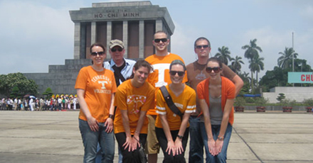 A group of students pose for a photo in UT shirts with a large monumen in the background